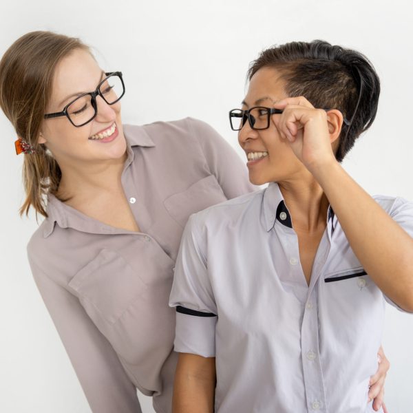 Positive women embracing and looking at each other. Multiethnic homosexual couple. Lesbian couple or women friendship concept. Isolated front view on white background.