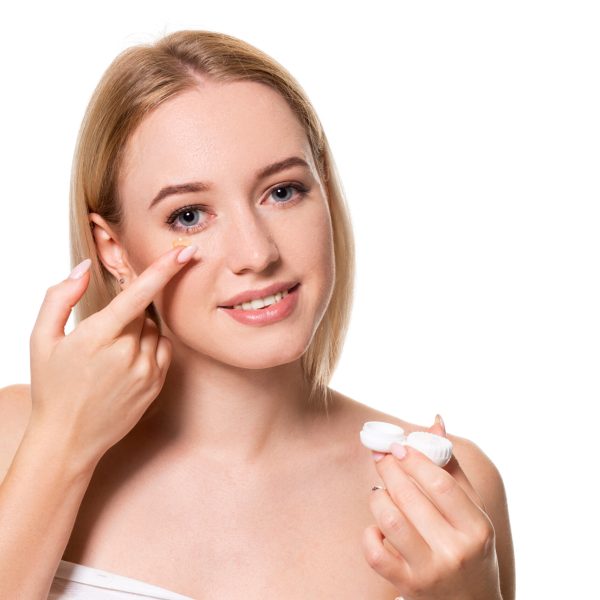 Young woman holding contact lenses cases and lens in front of her face on white background. Eyesight and ophthalmology concept.